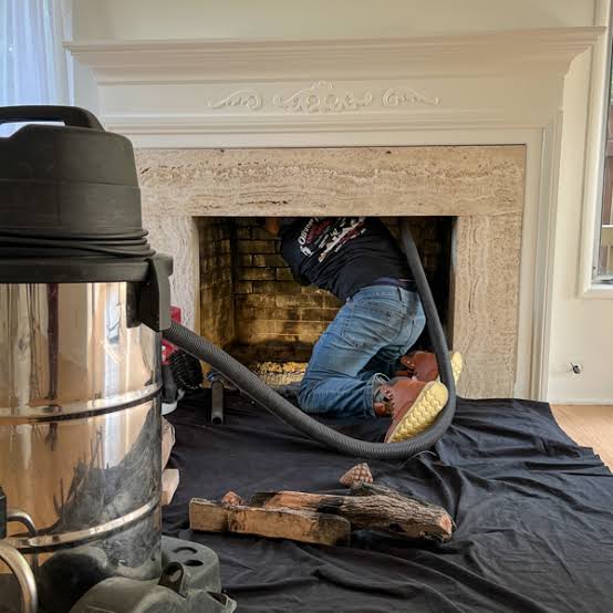 Technician working inside a fireplace with a stainless vacuum in the foreground