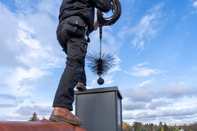 Sweep on a rooftop lowering a weighted round brush into a chimney top