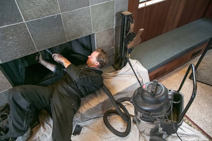 Technician lying on his back reaching into a fireplace smoke chamber